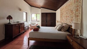 Un dormitorio con techo de madera, una cama con almohadas, un aparador, una silla y una ventana.