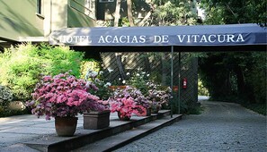 A hotel entrance with a sign reading "HOTEL ACACIAS DE VITACURA". There are potted plants with pink flowers in front of the entrance. - Hotel Acacias de Vitacura (Santiago)