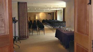 Un salón de conferencias con filas de sillas y una mesa con vasos, indicando una preparación para una reunión o evento.