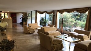 Ein geräumiges Wohnzimmer mit einer Sofagarnitur, einem Couchtisch und großen Fenstern mit Vorhängen.