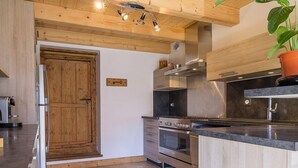 Une cuisine moderne avec des poutres en bois au plafond, un îlot central et des appareils électroménagers intégrés.