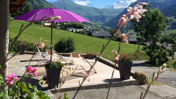 Une terrasse avec des meubles d’extérieur, un parasol violet et une vue sur des montagnes enneigées.