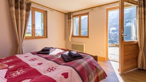 Une chambre avec un grand lit, deux fenêtres et une porte donnant sur un balcon.