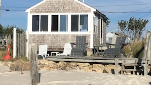 Una casa de playa con un amplio patio, mobiliario exterior y vista al océano.