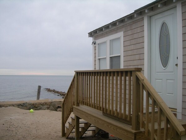Una casa de playa con una terraza de madera que da a una puerta con ventana.