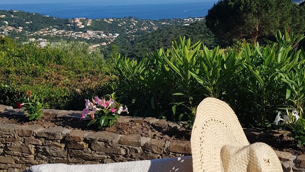 Una silla de playa con sombrero de paja, con vistas a un paisaje costero con casas y vegetación.