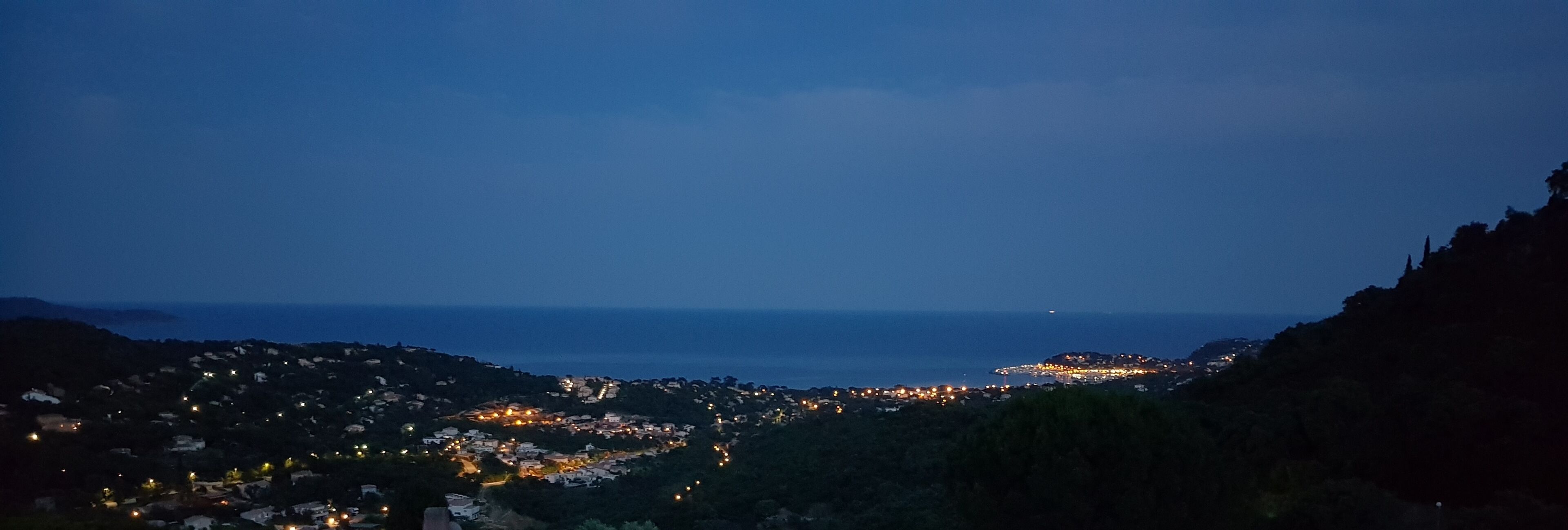 A coastal town at dusk with visible buildings and a clear view of the sea.