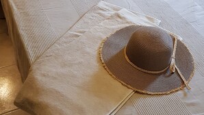 Una cama bien hecha con un edredón color beige y almohadas, un sombrero tejido sobre un taburete pequeño, y una almohada con estampado de mapa.