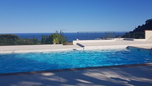 Una piscina con vistas al mar, rodeada por una terraza y una valla.
