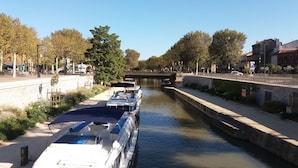 Ein Kanal mit Booten am linken Ufer, einer Steinbrücke in der Mitte und Gebäuden auf der rechten Seite.