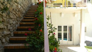 Eine Steintreppe führt zu einem Balkon mit einem Pool, umgeben von Blumentöpfen und Blumen.