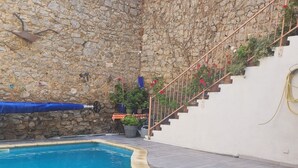 Ein Schwimmbecken mit einer Steinmauer und einer Treppe, die zu einer weißen oberen Ebene führt.