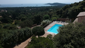 A pool with a wooden deck, surrounded by lush greenery and overlooking a coastal area with boats and hills. - Brand new villa with secured pool, panoramic view of sea and mountain, quiet (Zonza)