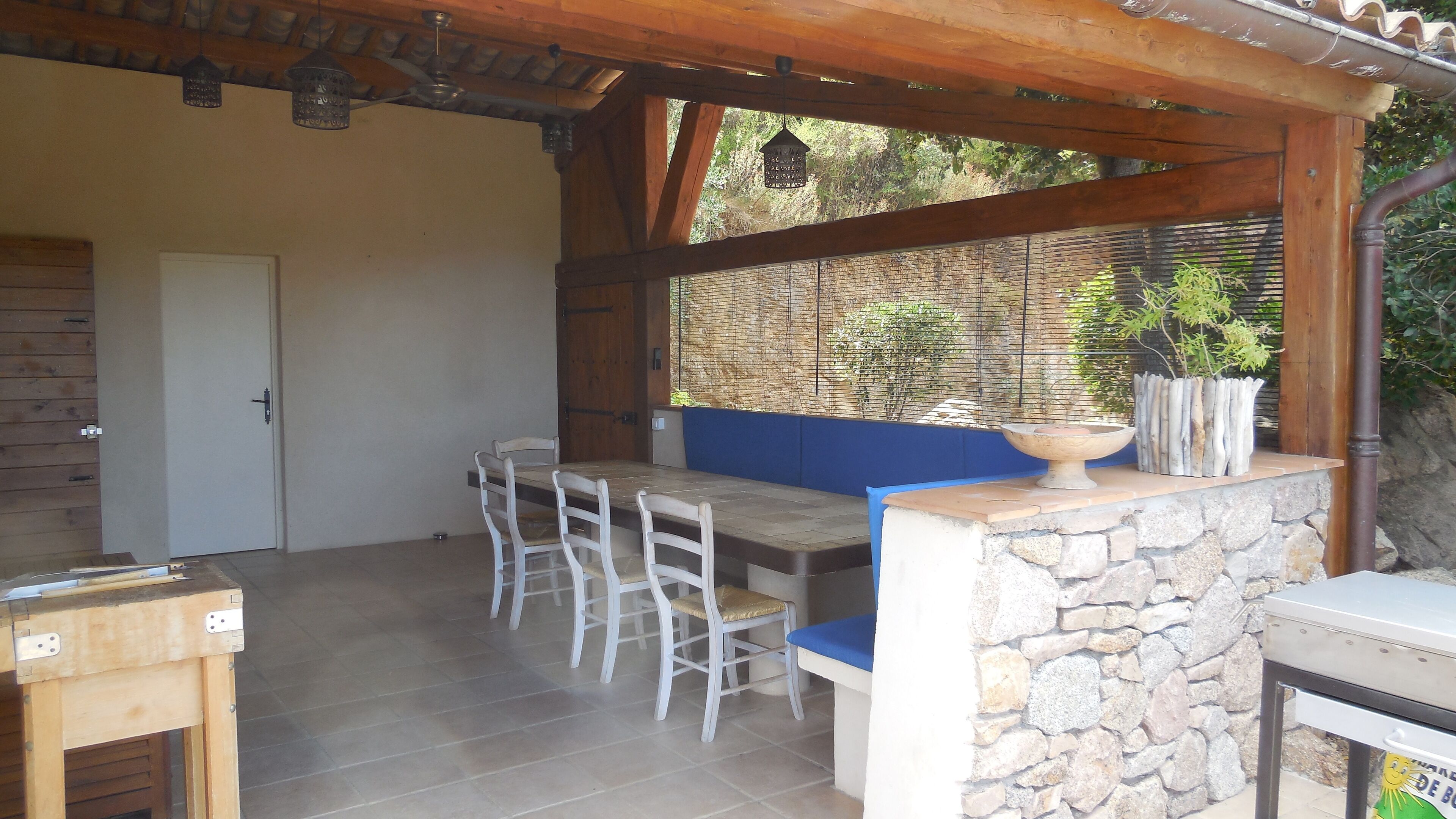 Eine Terrasse im Freien mit einer Steinsitzbank, einem Holztisch und einer hängenden Leuchte.