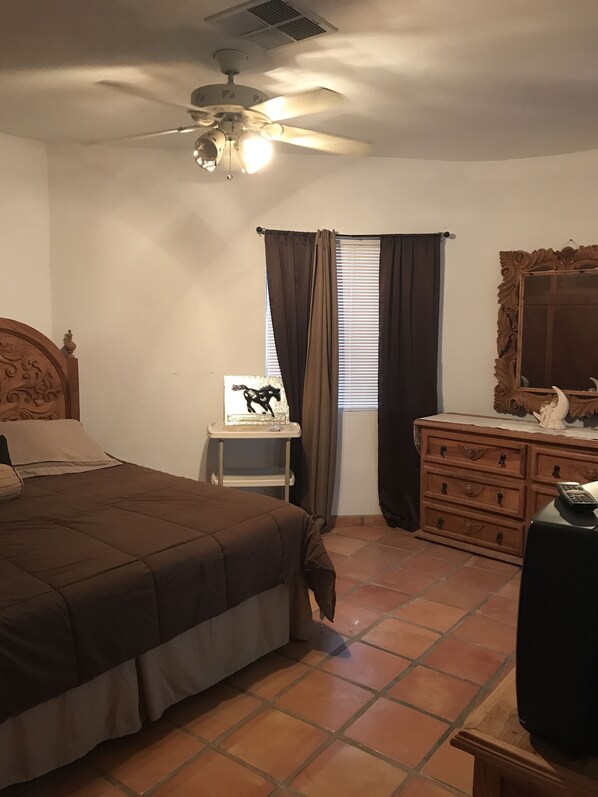 A bedroom with a bed, a dresser, a nightstand, a ceiling fan, and a window with curtains.