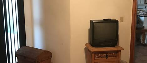A living room with a television on a wooden stand, a wooden chest, and a clock on the wall.