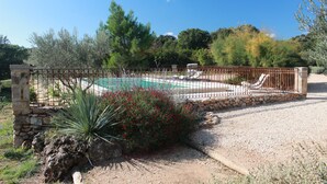 A pool area with a stone wall, a metal fence, and a stone bench. - Gite with a high standard of comfort between the garrigue and the provence (Argelliers)