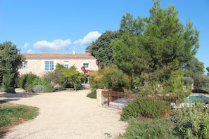 Un bâtiment en pierre avec un toit en tuiles, entouré d’une allée gravillonnée et d’une clôture en métal.
