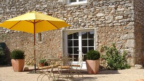 A stone building with a patio area featuring lounge chairs, a table, and an umbrella. - Gite with a high standard of comfort between the garrigue and the provence (Argelliers)
