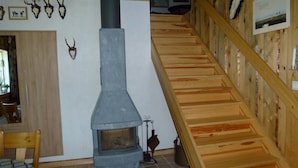 Un intérieur rustique avec une cheminée en pierre, un escalier en bois et des crânes d’animaux accrochés au mur.