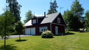 Une grange rouge avec deux portes de garage, entourée d’une pelouse bien entretenue et d’arbres.