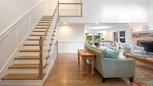 A spacious living area with a wooden staircase, a sofa set, and a fireplace. - Brand New in the Heart of East Hampton Village with Pool (East Hampton)