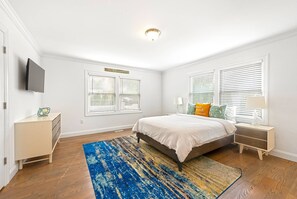 A bedroom with a bed, nightstands, a TV, and a window with blinds. - Brand New in the Heart of East Hampton Village with Pool (East Hampton)