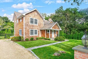 A two-story house with a front porch, a small attached garage, and a well-maintained lawn. - Brand New in the Heart of East Hampton Village with Pool (East Hampton)