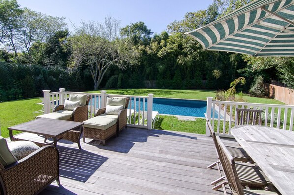 A wooden deck with wicker furniture, a pool, and a white fence. - Brand New in the Heart of East Hampton Village with Pool (East Hampton)