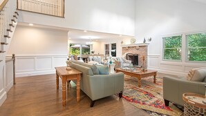 A spacious living room with a high ceiling, a fireplace, and a staircase leading to an upper level. - Brand New in the Heart of East Hampton Village with Pool (East Hampton)