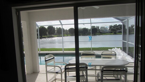 A poolside area with a table and chairs, a view of a lake, and a glass door leading to the pool. - Beachwalk Isles Executive 4 Bedroom Lakeside Pool Villa (Ft Myers)