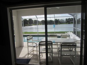 Un espace aménagé au bord de la piscine, avec une table et des chaises, une vue sur un lac et une porte vitrée donnant accès à la piscine.
