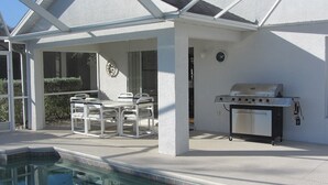 A covered outdoor area with a pool, a grill, and a table with chairs. - Beachwalk Isles Executive 4 Bedroom Lakeside Pool Villa (Ft Myers)