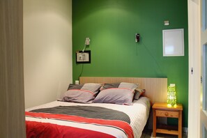 A bedroom with a bed, pillows, a nightstand with a lamp, and a wall-mounted telephone.
