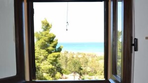 Una habitación con cama, una mesita de noche con lámpara y ventana con vistas a árboles y al mar.