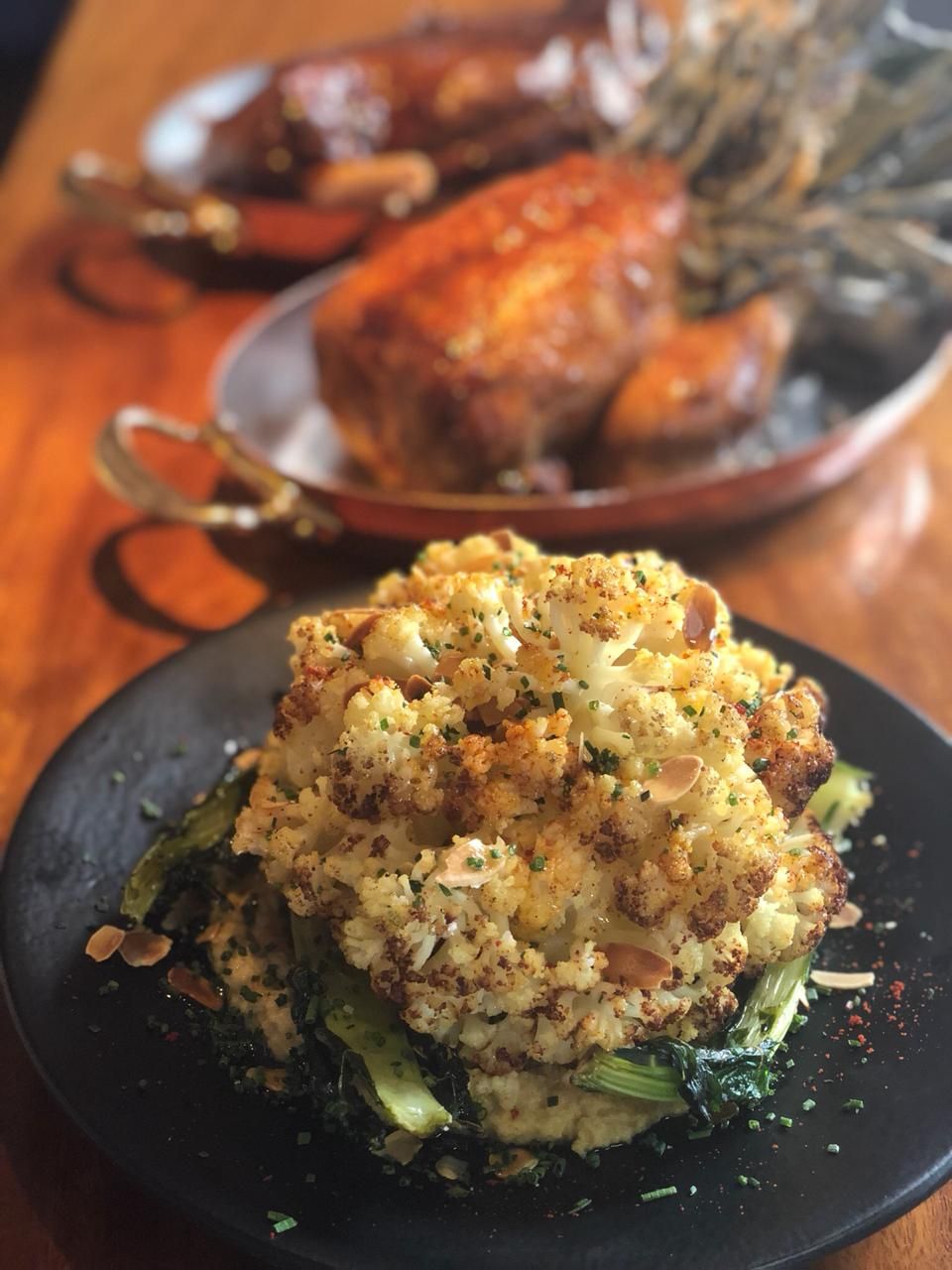 A plate of roasted cauliflower with herbs and a roasted chicken in the background.
