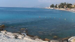 A coastal view with clear blue waters, rocky shoreline, and a distant cityscape. - Beautiful farm house with pool, open spaces  and amazing sea views  (Bordighera)