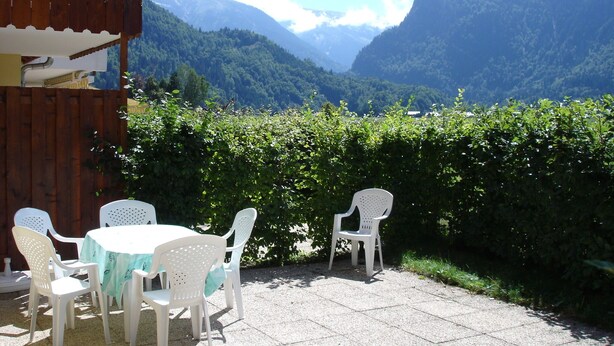 Eine Terrasse im Freien mit Tisch und Stühlen, einem Holzzaun und Blick auf Berge und grüne Landschaft.