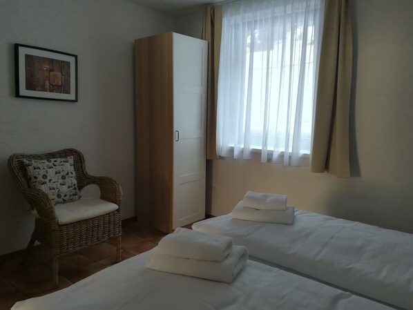 A room with two beds, a wicker chair, a wardrobe, and a window with curtains. - Wellness privát Štyri Lipy (Liptovske Revuce)