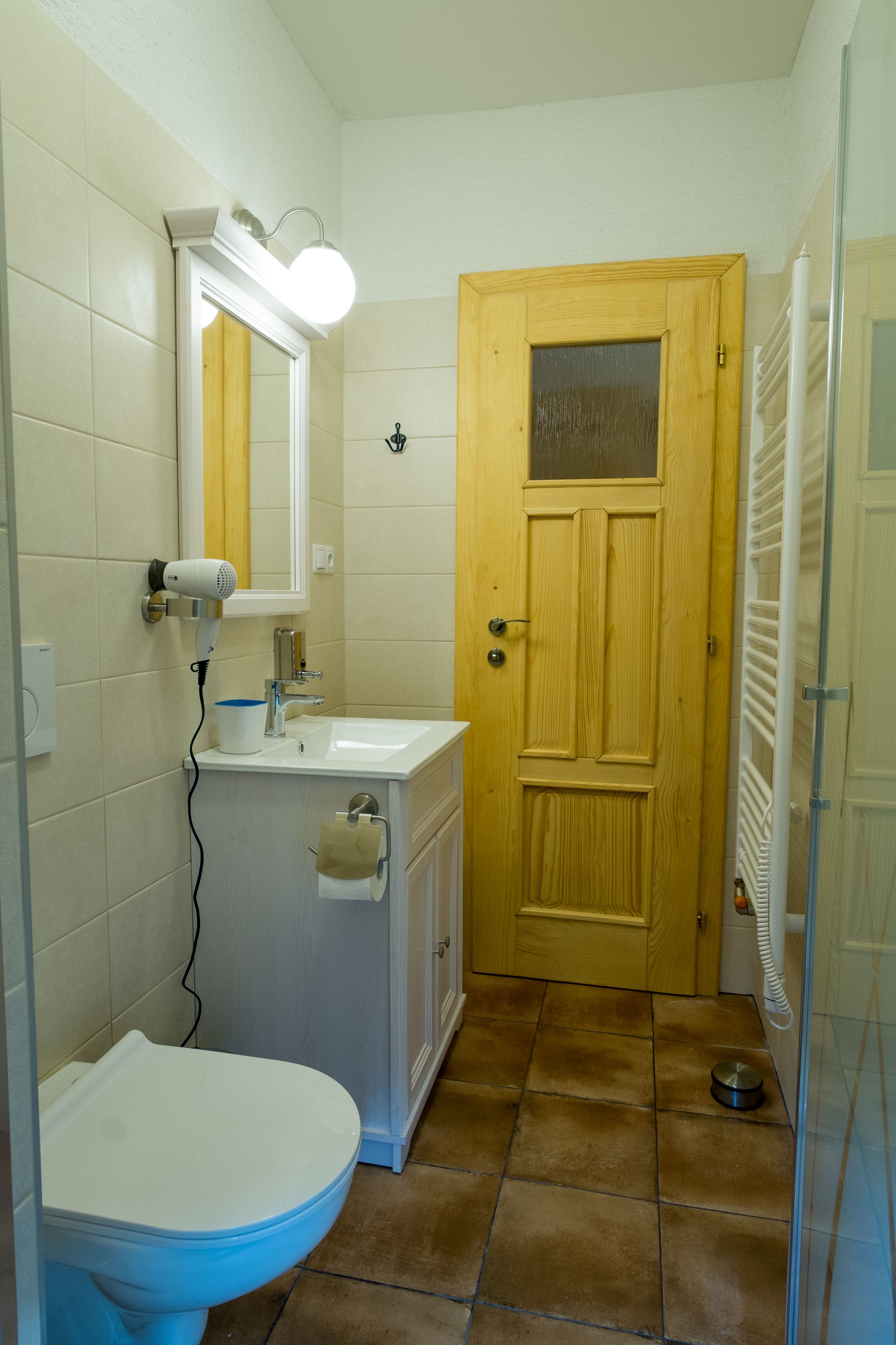 A bathroom with a toilet, sink, mirror, and a wooden door.
