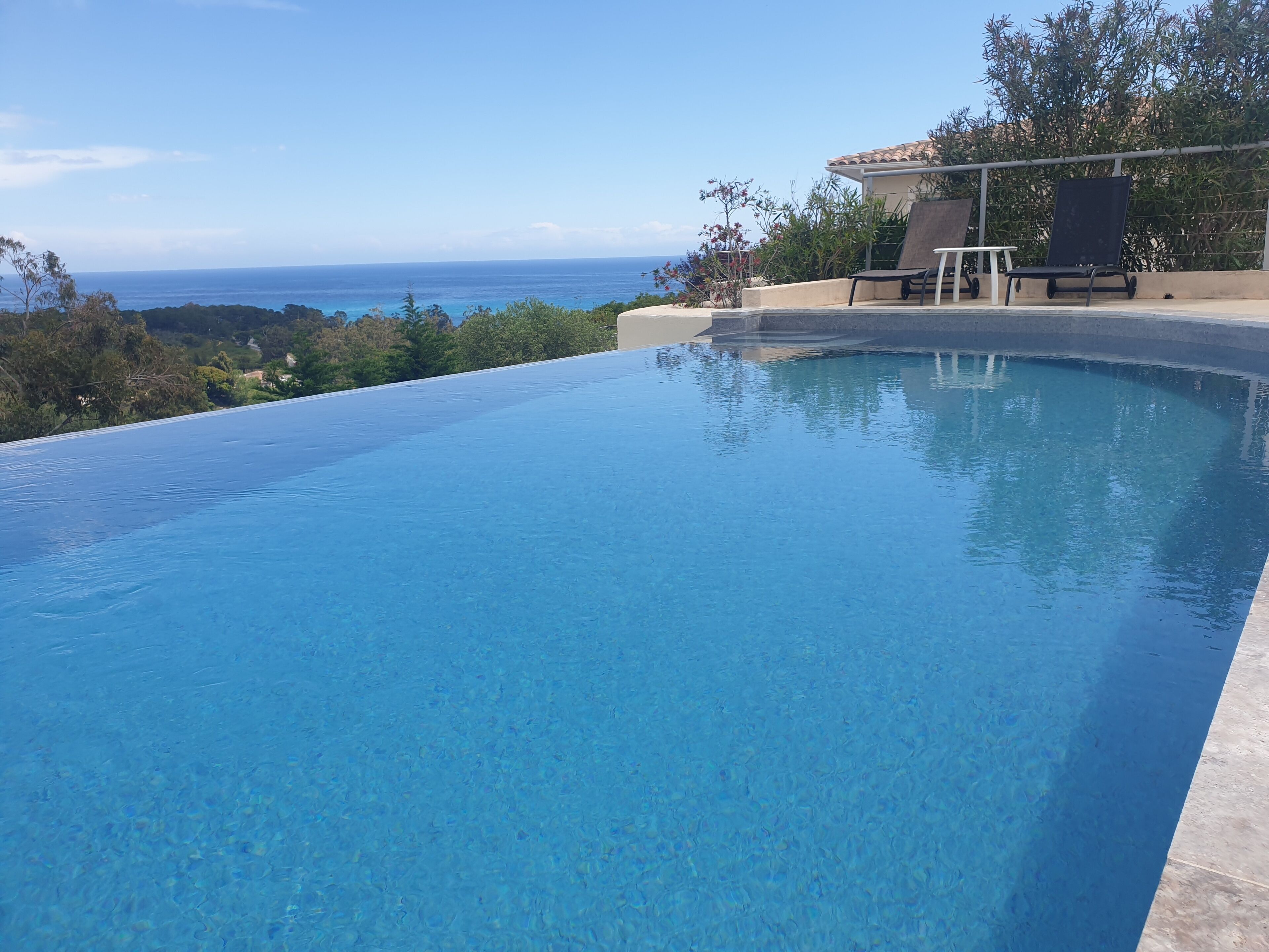 A clear blue infinity pool with a view of the ocean and hills.