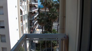 Blick vom Balkon auf ein mehrstöckiges Gebäude mit Balkonen, Palmen und geparkten Autos.