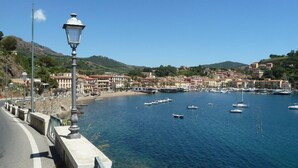 A coastal town with clear blue waters, boats, and buildings along the shore. - Blue harbor lovely apartment with terrace above the beach. (Porto Azzurro)