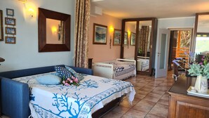 A bedroom with a bed, a bedside table, a mirror, and a view of the garden. - Blue harbor lovely apartment with terrace above the beach. (Porto Azzurro)