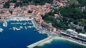 An aerial view of a coastal town with a marina, buildings, and greenery. - Blue harbor lovely apartment with terrace above the beach. (Porto Azzurro)