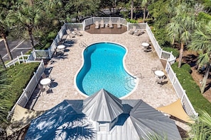 Vista aérea de una piscina rodeada por una terraza con sillas de descanso y una zona de estar cubierta.