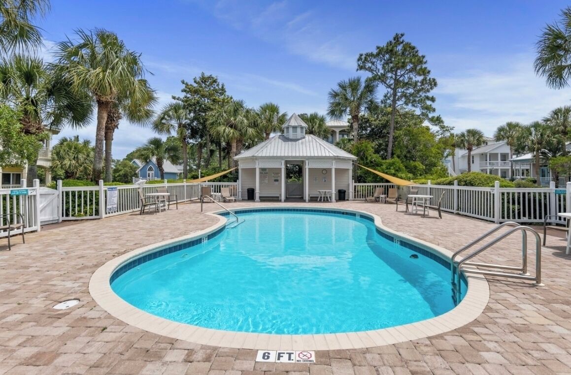 A swimming pool with a 6 ft depth limit, surrounded by a white fence, palm trees, and a gazebo-like structure.