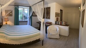 A bedroom with a bed, a chair, a bedside table with books, and a window with curtains.