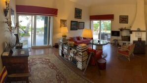 A spacious living area with a large window, a red sofa, a coffee table, and a bookshelf filled with books.