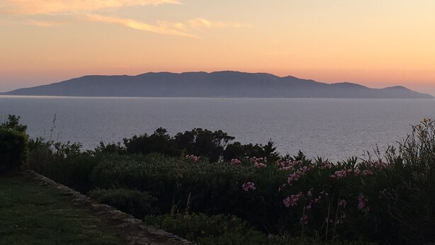 Paesaggio costiero con vista sul mare e montagne lontane al tramonto.